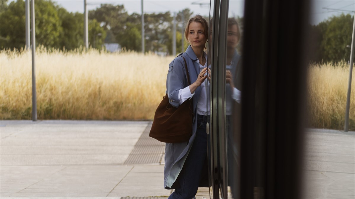 Жена во син капут и со голема торба ја отвора вратата на концепт автомобилот Dacia Hipster, со природен пејзаж во позадина.