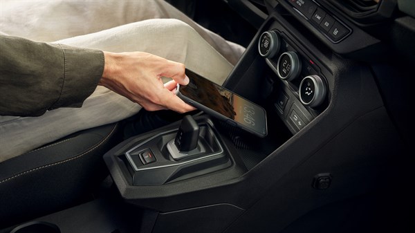 Внатрешност на Dacia Jogger со лице кое го става својот паметен телефон на вградениот безжичен полнач во централната конзола.