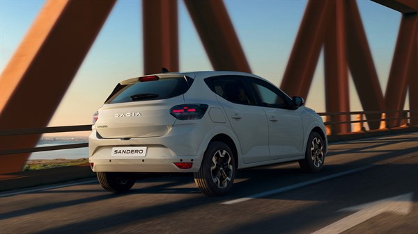 Dacia Sandero во бела боја фотографирана одназад како вози преку метален мост, со истакнати нови задни светла и линии на каросеријата.