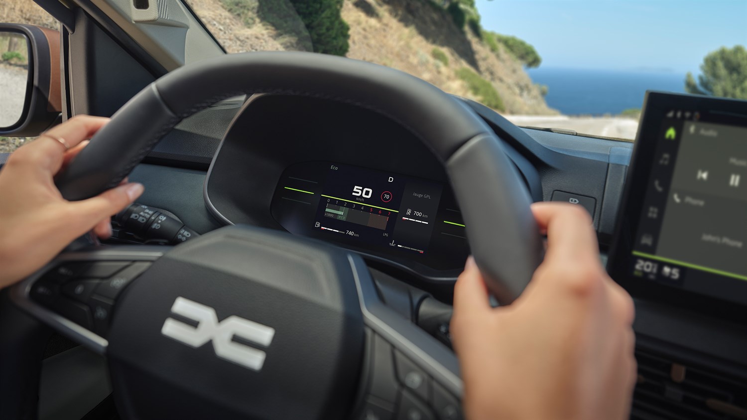 озачот го држи управувачот во Dacia Sandero, а дигиталната инструмент табла прикажува информации за брзината, опсегот и режимот на возење.