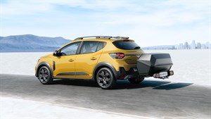 Жолто возило Dacia Sandero прикажано од задната страна на отворен пат, со приколка прикачена на кука за влечење.