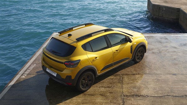 Dacia Sandero во жолта боја, фотографирано одгоре, паркирано покрај морето на бетонска површина.