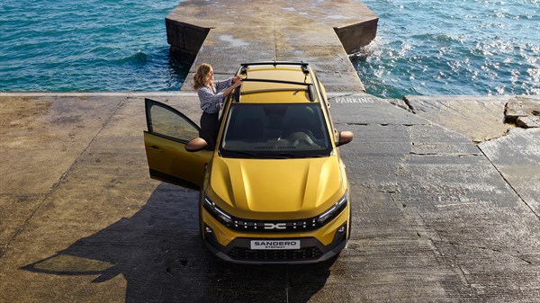 Жолт Dacia Sandero Stepway фотографиран од страна покрај морето, паркиран на бетонска површина со планински пејзаж во позадина.